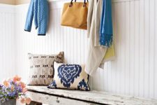 a bright shabby chic entryway with white shiplap, a wooden bench, baskets, pillows and a blue clothes hanger
