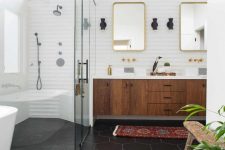 a chic mid-century modern bathroom with black hex tiles on the floor, a boho rug, a wooden floating vanity and touches of gold