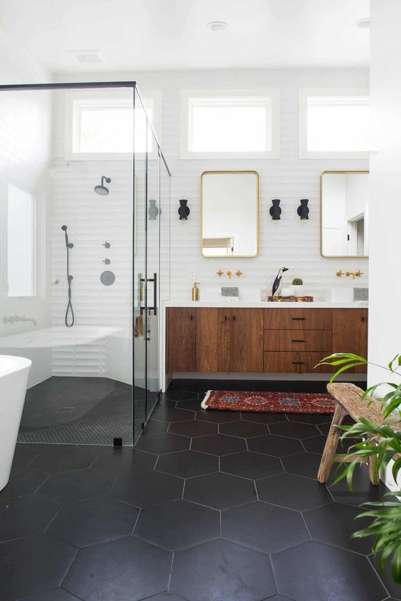 a chic mid-century modern bathroom with black hex tiles on the floor, a boho rug, a wooden floating vanity and touches of gold