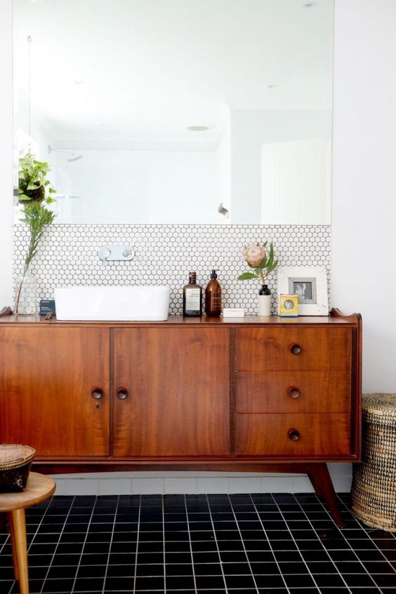 a chic mid-century modern space with white hex tiles and black usual ones, a rich stained vnaity and a statement mirror