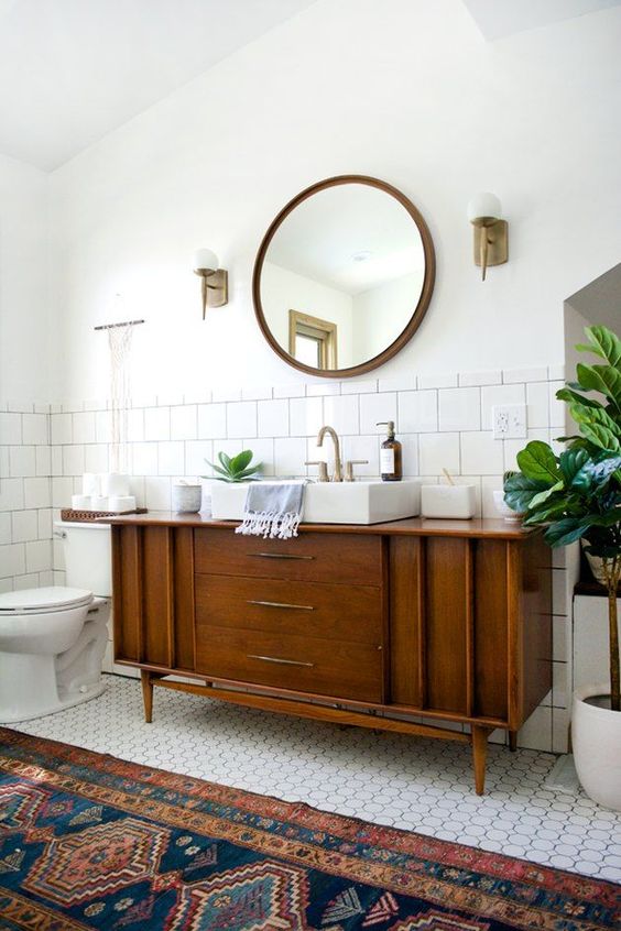 a classic mid-century modern bathroom with white square and penny tiles, a boho rug, a wooden vanity and touches of brass