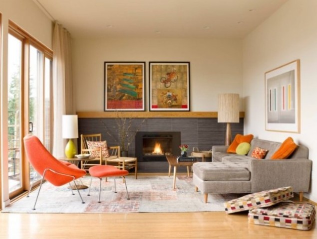 a colorful mid-century modern living room with a built-in fireplace, a grey sectional, a fiery red chair, a wooden chair, a low table and colroful artworks