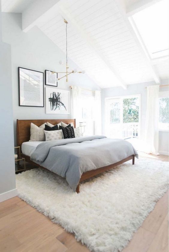 a light-filled mid-century modern bedroom with a rich-stained wooden bed, a fluffy rug, a geometric chandelier and a gallery wall
