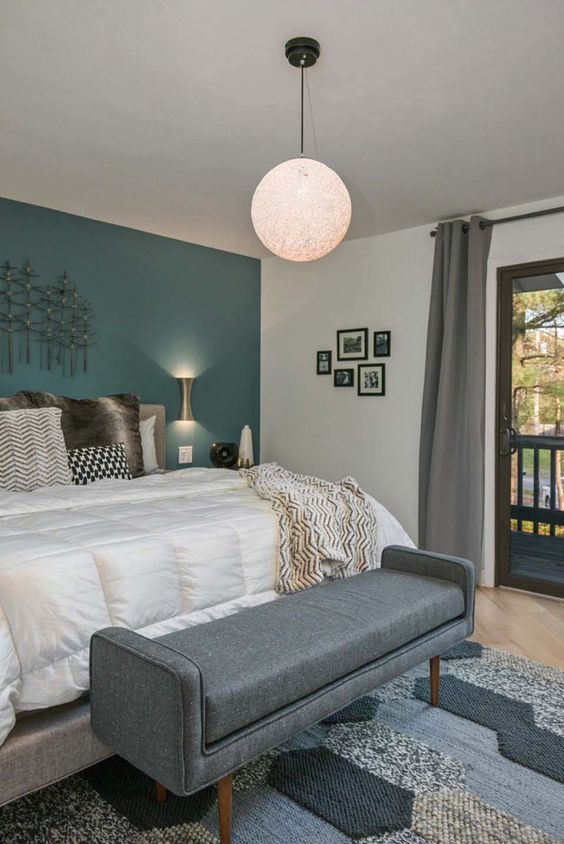 a mid-century modern bedroom with a teal statement wall, a grey bench and a globe pendant lamp