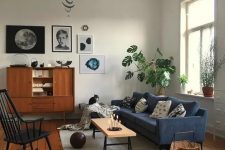 a mid-century modern living room with a navy sofa, a black rocker, potted plants, a stylish gallery wall and some cat furniture