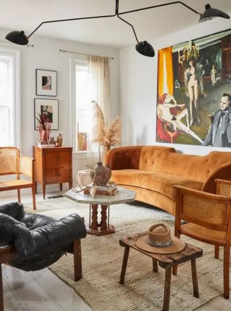 a modern and boho living room with a rust-colored sofa, rattan chairs, wooden and leather furniture and a statement artwork