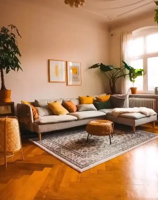 a modern warm-toned living room with blush walls, a grey sectional, mustard and yellow pillows and potted plants