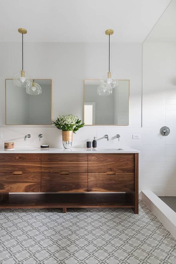 a neutral mid-century modern bathroom with white and mosaic geo tiles, a wooden vanity and chic pendant lamps plus mirrors in gold frames