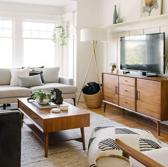 a simple mid-century modern living room with a creamy sofa, a stained TV unit and coffee table, printed pillows and some greenery
