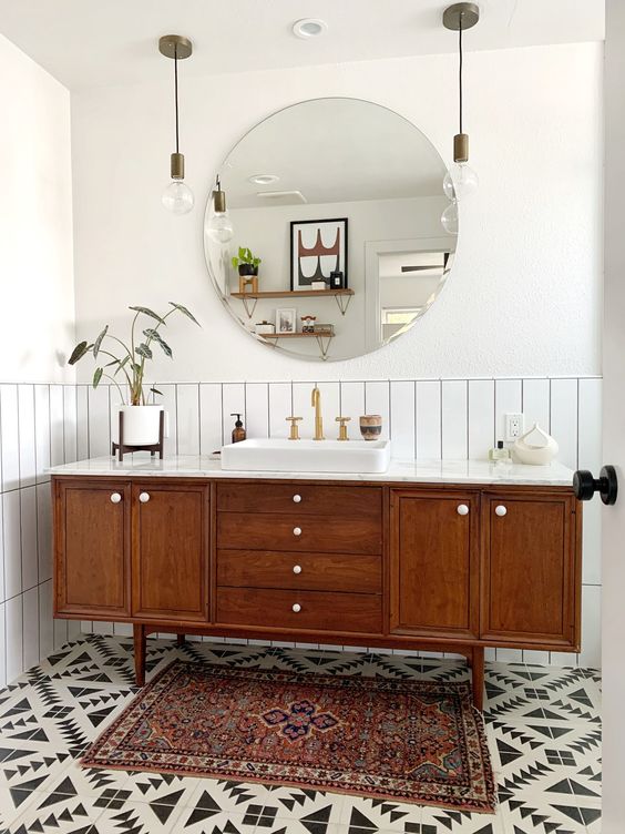 a stylish mid-century modern bathroom with whiet skinny tiles, geo tiles on the floor, a boho rug, a wooden vanity and pendant lamps