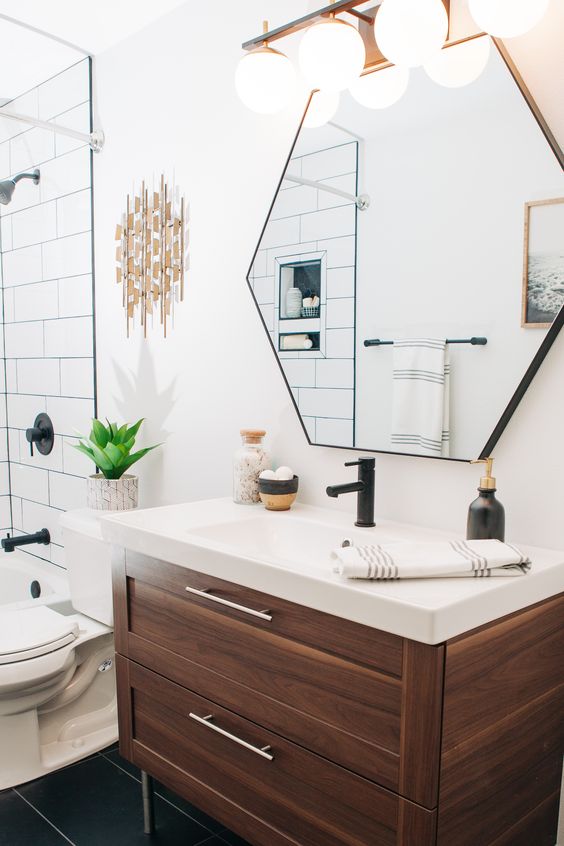 a stylish mid-century modern bathroom with white and black tiles, a hexagon mirror, a wooden vanity and touches of brass