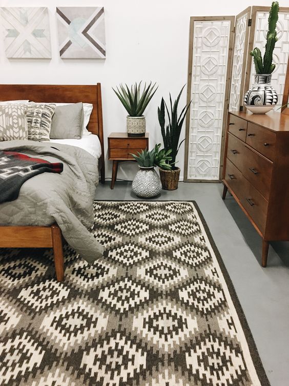 a stylish mid-century modern bedroom with a geometric rug, rich-stained furniture, potted greenery and artworks