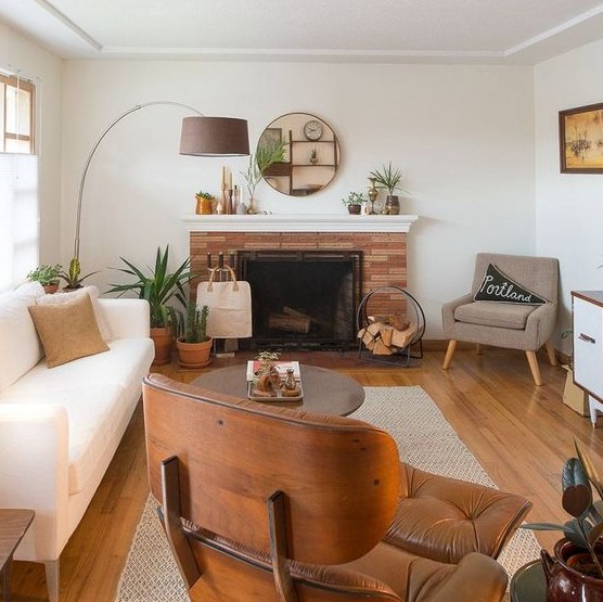 a welcoming mid-century modern living room with a creamy sofa, a tan and an maber chair, a coffee table, a fireplace clad with brick and a cool floor lamp