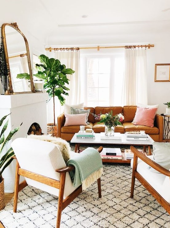 a welcoming mid-century modern lviing room with a non-working fireplace, an amber leather sofa, white chairs, a low coffee table, a mirror and pastel pillows