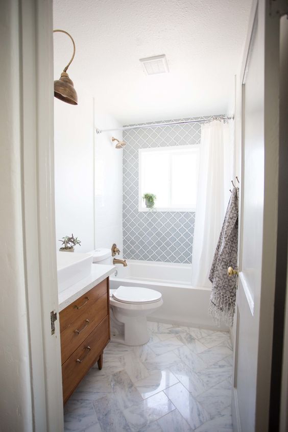 an airy mid-century modern bathroom with grey Moroccan tiles, white marble ones, a wooden vanity and touches of brass