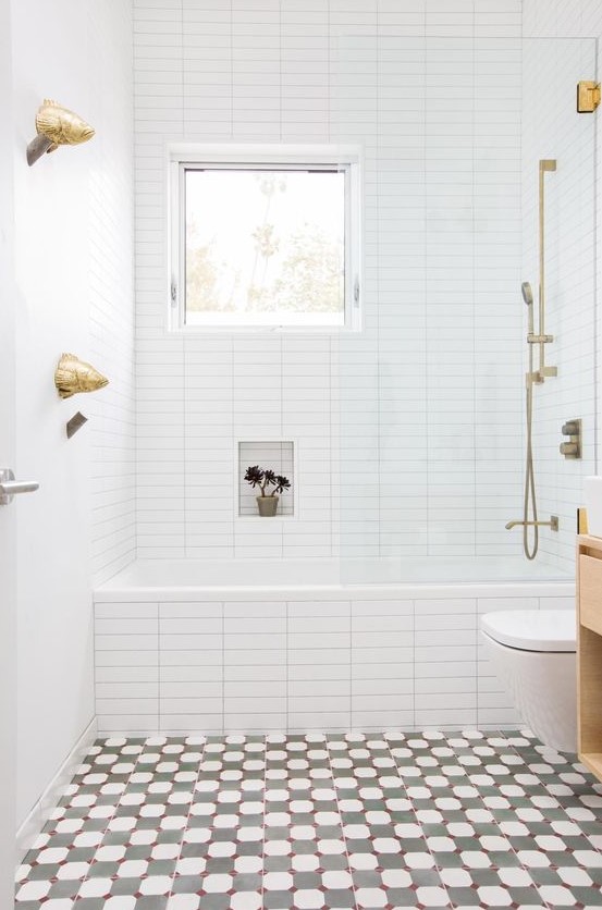 a bright bathroom with a mosaic floor, white tiles with built-in shelves, a window and gold hardware