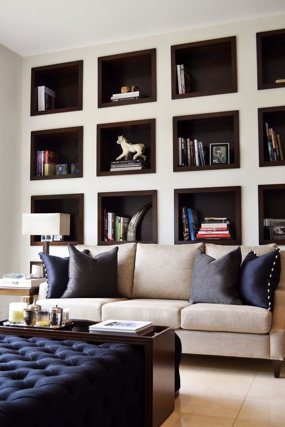 a chic and elegant living room done in neutrals with touches of navy, with a whole wall taken by niche shelves to store and display