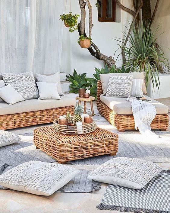 a coastal outdoor space with wicker outdoor furniture and a side table, neutral teixtiles and lots of plants around