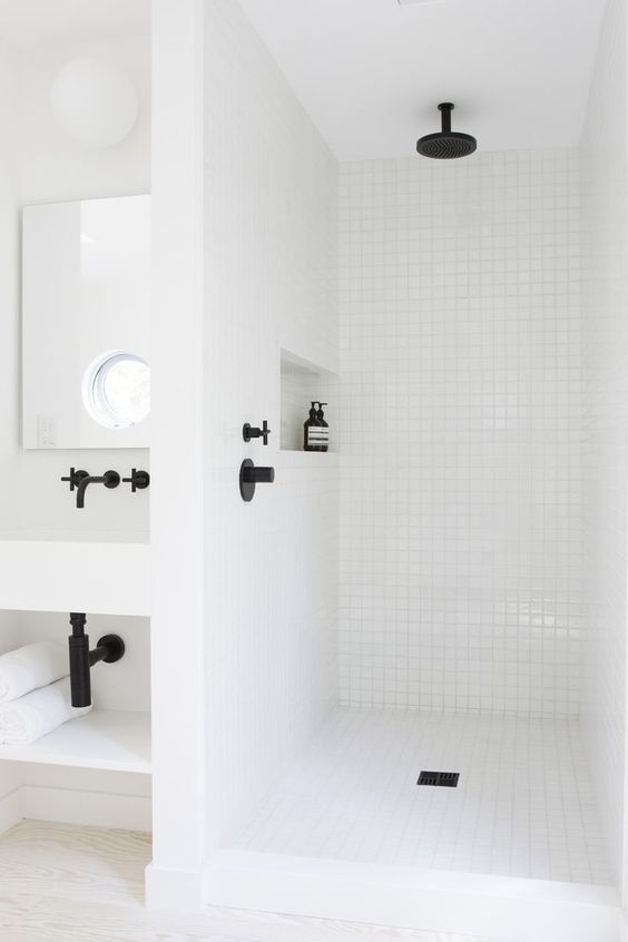 a contemporary white bathroom clad with square tiles and black fixtures, a niche shelf, a wall-mounted vanity is stylish