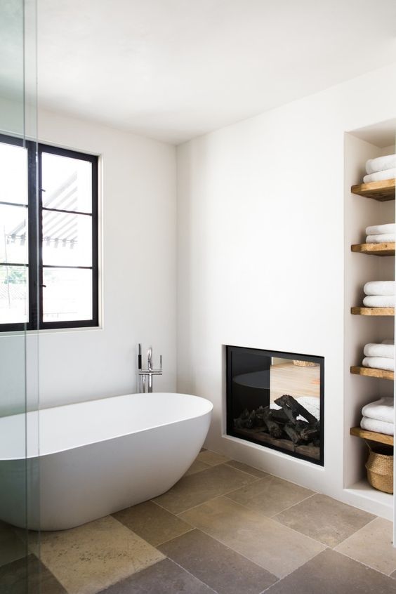 a contemporary white bathroom with a beige tile floor and a fireplace, with a niche with wooden shelves is cool