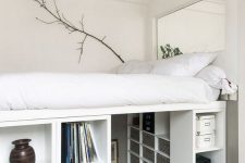 a creative tiny bedroom with a platform bed placed on storage units that create a whole wardrobe under it