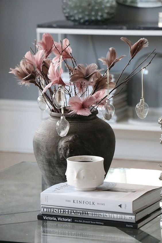 a dark vase with branches with pink and mauve feathers and glass egg ornaments with feathers inside