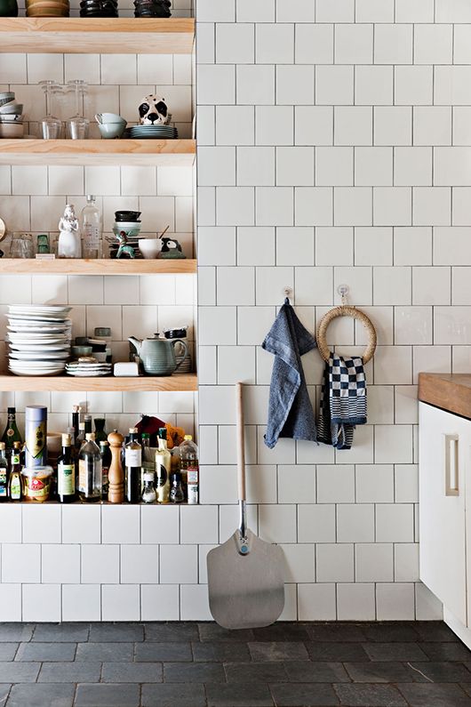 a kitchen clad with white square tiles and with niche shelves that are used instead of cabinets to store everything needed