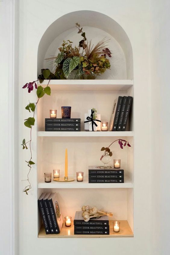 a lovely arched niche with shelves displaying books, candles and a potted plant is a stylish idea for a any space