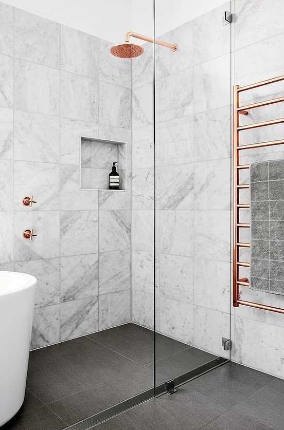 a marble tile bathroom with a dark floor, a tub, a shower and copper hardware for a chic and bold look