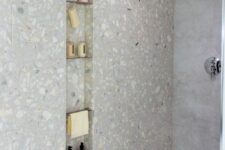a minimalist shower space clad with stone tiles and with a long and narrow niche with metal shelves is a cool nook