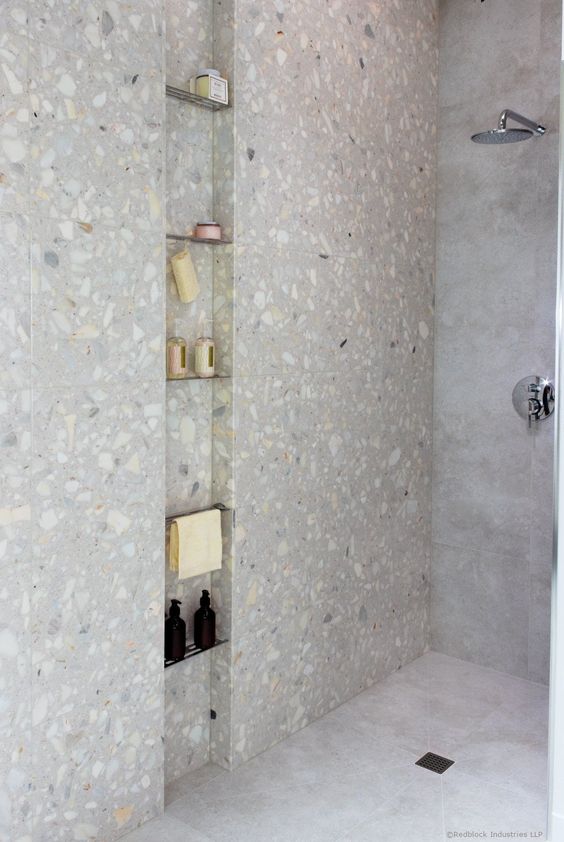 a minimalist shower space clad with stone tiles and with a long and narrow niche with metal shelves is a cool nook