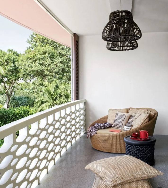 a modern balcony with a double wicker chair with lots of pillows, a black side table, black wooden pendant lamps and some jute pillows