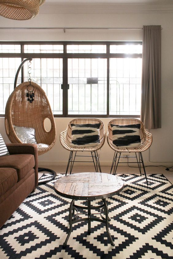 a modern living room with a brown sofa, a round table with a wooden tabletop, wicker chairs, a wicker pendant chair is amazing