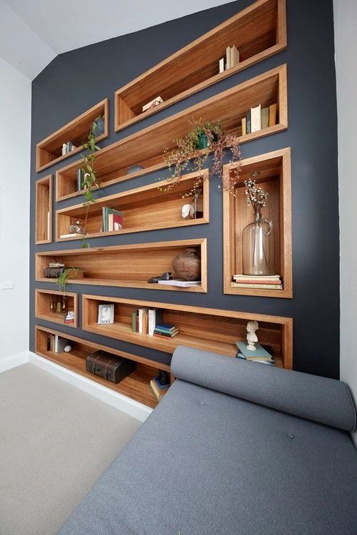 a modern living room with a graphite grey accent wall dotted with stained wood niche shelves used as a large display