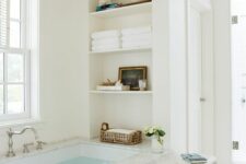 a neutral airy bathroom with a bathtub and niche shelves by its side is a cool idea, there you can store anything you want