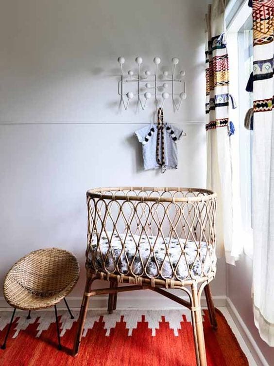 a pretty boho nursery nook with a wicker crib and a small round chair, colorful textiles and a rack for hanging clothes