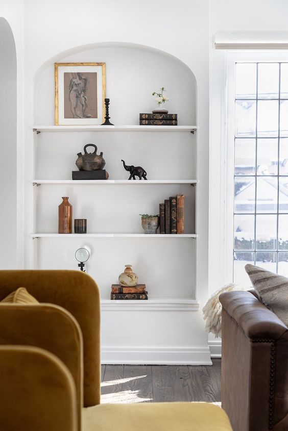 a refined living room with a large niche in the wall featuring some shelves, books and decor is a gorgeous space