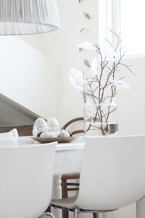 a sheer vase with branches decorated with white feathers and a wooden tray with black and white eggs