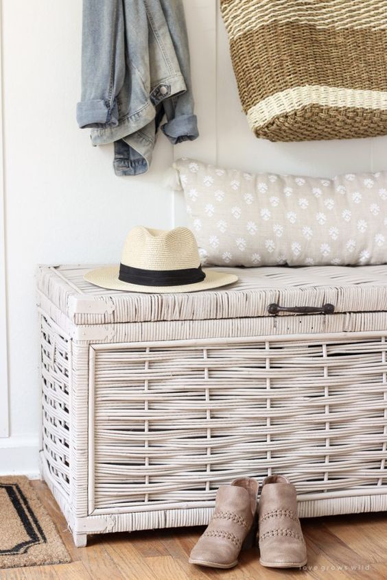 a small rustic entrywya with a wicker storage chest that doubles as a seat, a grey and white pillow, some pretty clothes and shoes
