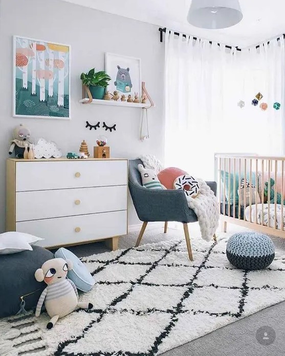 a Scandi nursery with bright touches - artworks, pillows, a pouf and a chair and some bright bedding in the crib is lovely