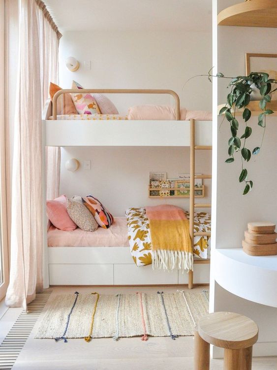 a Scandi shared girls' bedroom with a bunk bed, a desk with a wooden stool and some built-in shelves, pink and mustard textiles