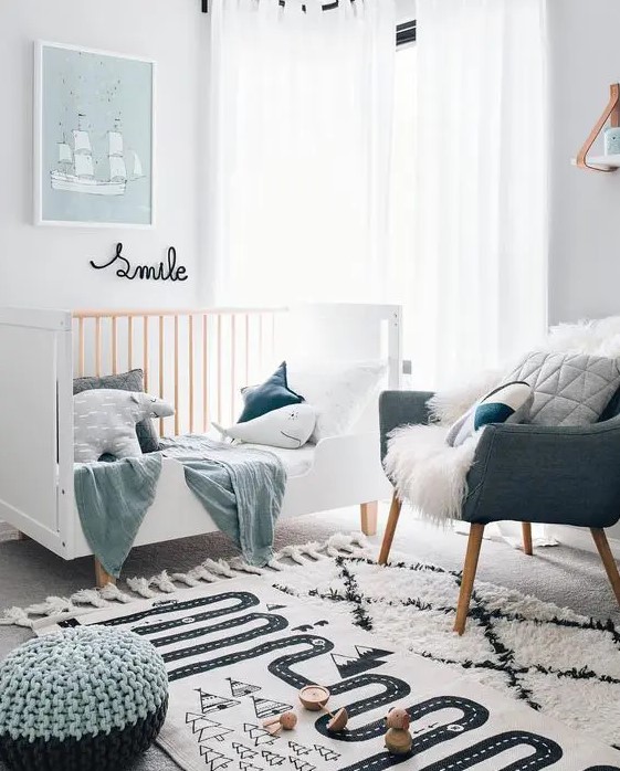 a Scandinavian nursery with a white crib, a grey chair, printed rugs and grey and blue textiles plus some art