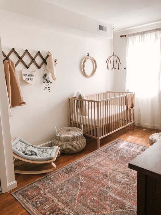 a boho gender neutral nursery with light stained furniture, a boho rug, a mobile and a littel rocker
