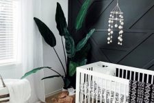 a boho nursery with a black geometric accent wall that stands out and make the whole space more stylish