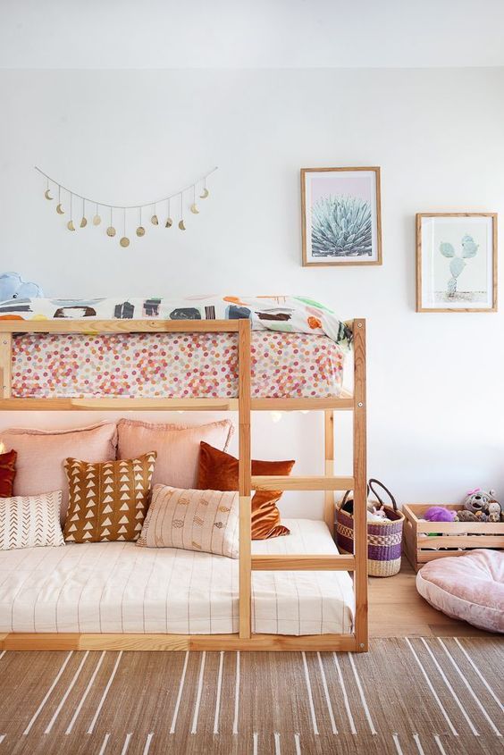 a boho shared girls' bedroom with a wooden bunk bed and printed bedding and pillows, a crate with toys, a gallery wall and a boho rug