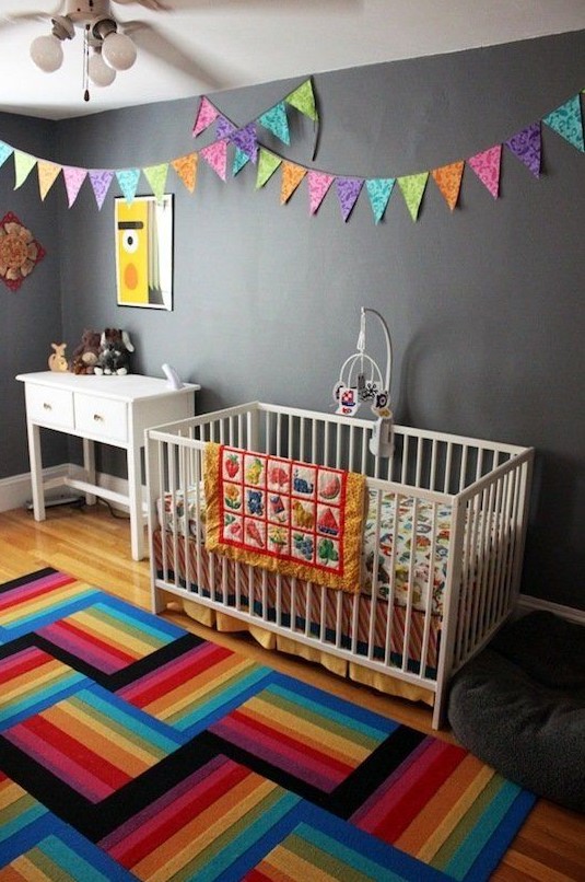 a bold nursery with grey walls but striped rugs, colorful buntings, colorful bedding and artworks for fun