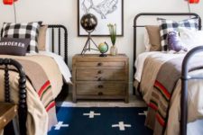 a bold shared teen boy bedroom with black beds, layered rugs, bright bedding, a gallery wall and red sconces