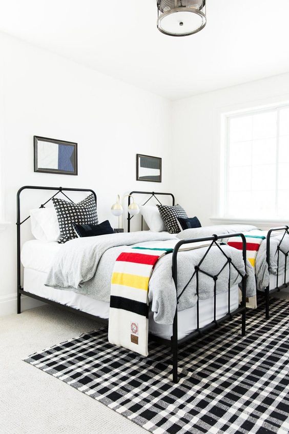 a bright shared boy bedroom with white walls, black beds, layered rugs and bright graphic bedding