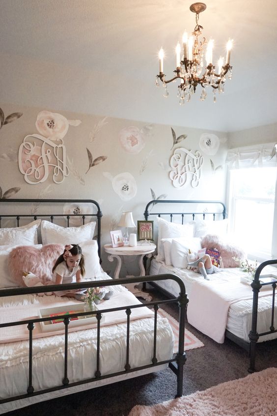 a chic farmhouse shared girls' bedroom with a floral accent wall and monograms, with metal beds and white and pink bedding, a round table as a nightstand