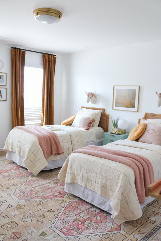 a chic shared girls' bedroom with a bright printed rug, cane headboard beds with pastel and mustard bedding, mustard curtains and a mint blue nightstand